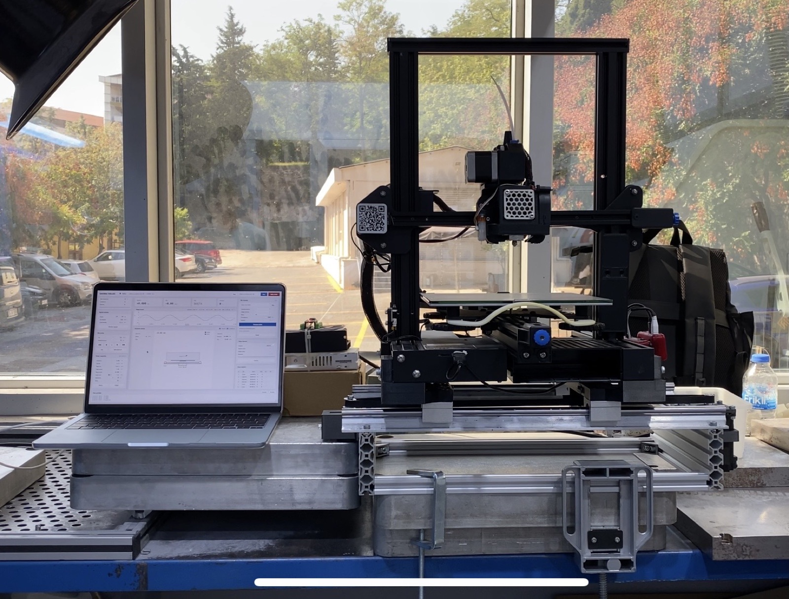 FDM printer on a single-axis vibration stage next to the control laptop in the laboratory.